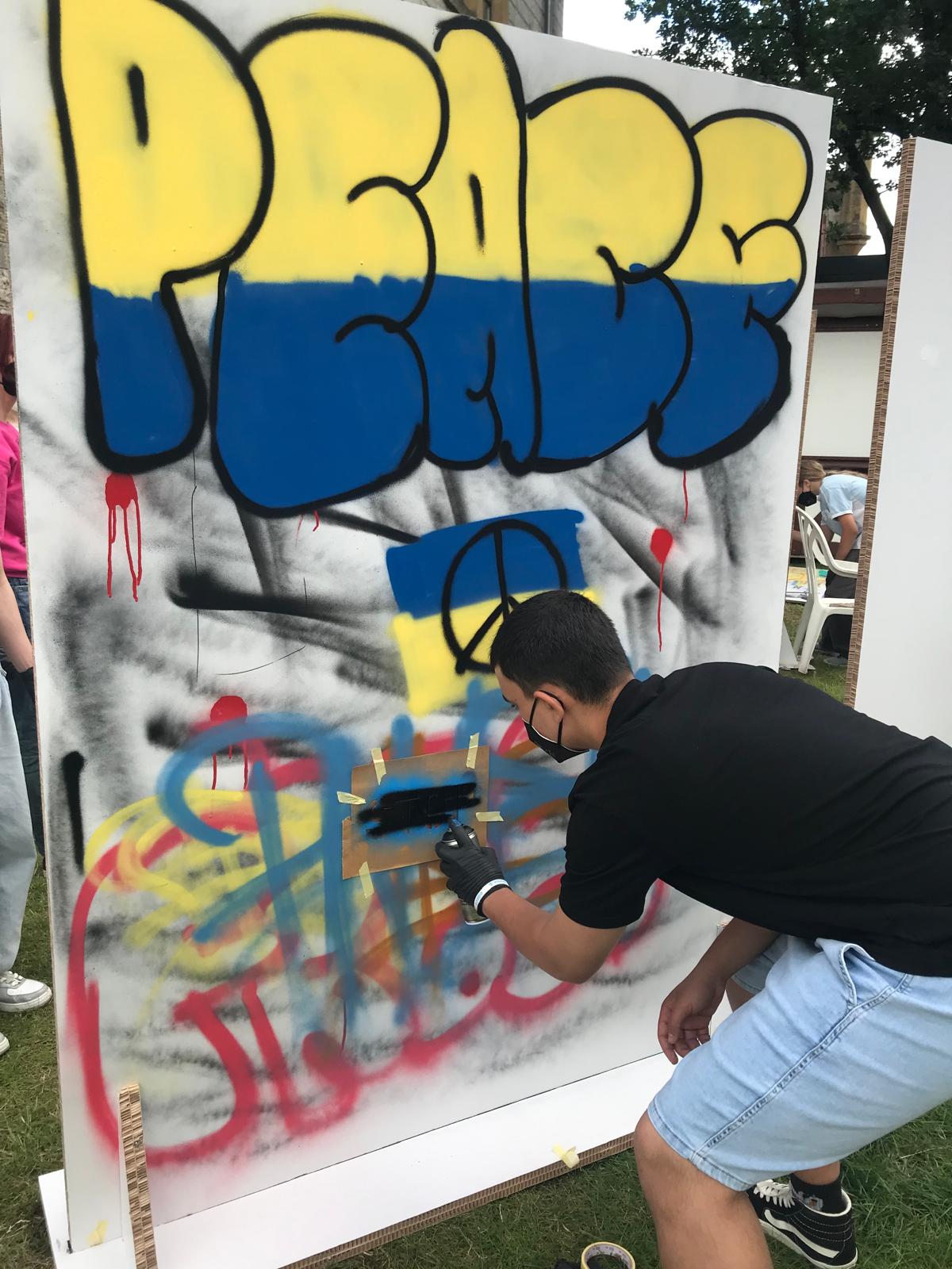 Eine Person sprüht ein Graffitistencil im Rahmen eines Workshops an die Wand.