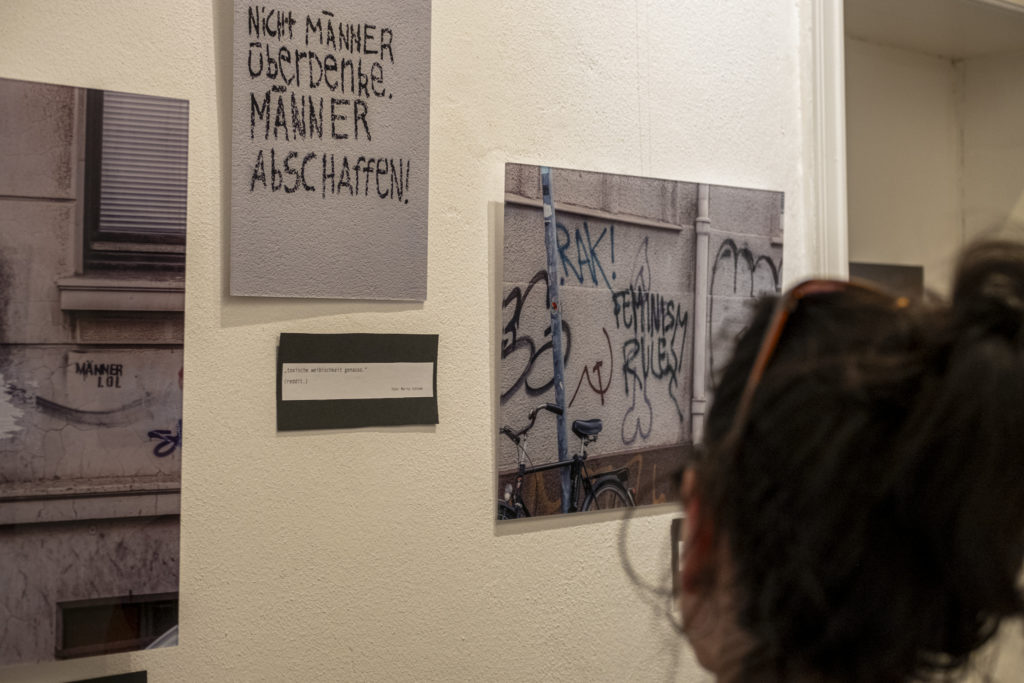 In einer Ausstellung sind Bilder an einer Wand zu sehen. Eine Person betrachtet diese.