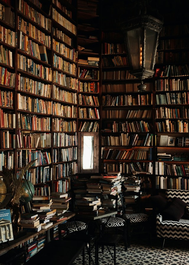 Abgedunkelter Raum mit Wänden voller alter Bücher und einem kleinen Fenster